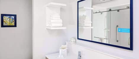 A modern bathroom with a large mirror, white shelves with towels, a toilet, and a sink.