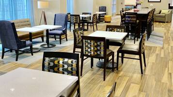Un vestíbulo de hotel con varias zonas de estar, que incluyen mesas y sillas, un sofá y una pequeña sala de comedor.