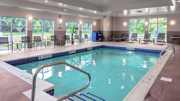 An indoor swimming pool with clear water, surrounded by lounge chairs and a sunbed area.