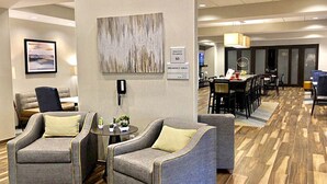 A hotel lobby with grey upholstered sofas, a breakfast area, and a maximum occupancy sign of 60.