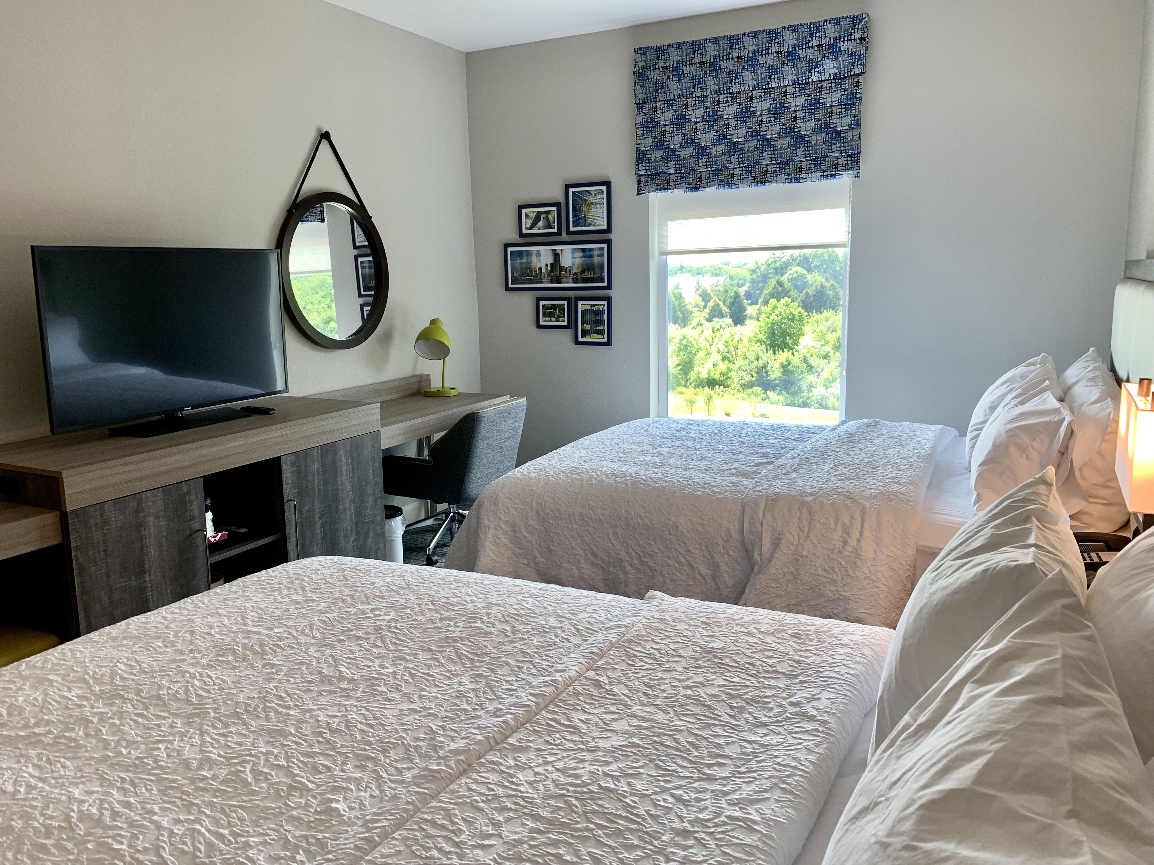 A hotel room with two beds, a desk with a TV, a mirror, and framed pictures on the wall.