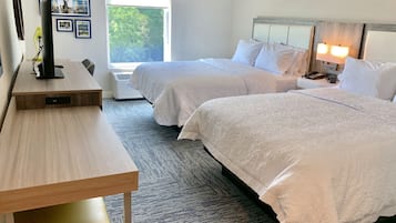 Habitación de hotel con dos camas, un escritorio y una ventana con vista a árboles.