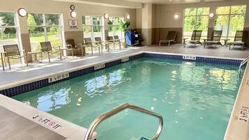 A swimming pool with a no diving sign, lounge chairs, and a clock on the wall.