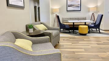 A modern hotel lobby with a seating area, a dining table, and a large painting on the wall.