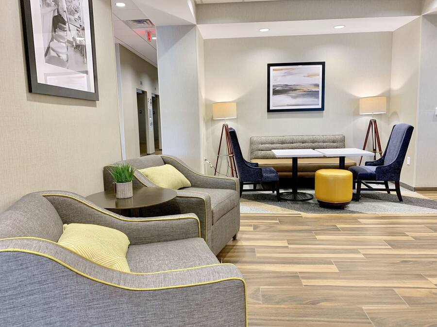 A modern hotel lobby with a seating area, a dining table, and a large painting on the wall.