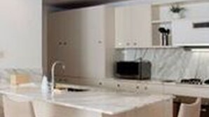 A modern kitchen with a central island, white cabinetry, and two bar stools. - Apartamentos en el Centro Histórico (Cartagena)