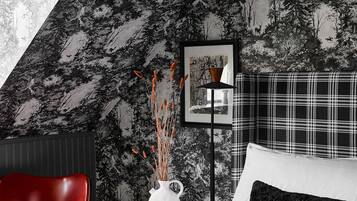 A bedroom with a bed, a red chair, a white vase with plants, a framed picture, and a black and white checkered blanket.