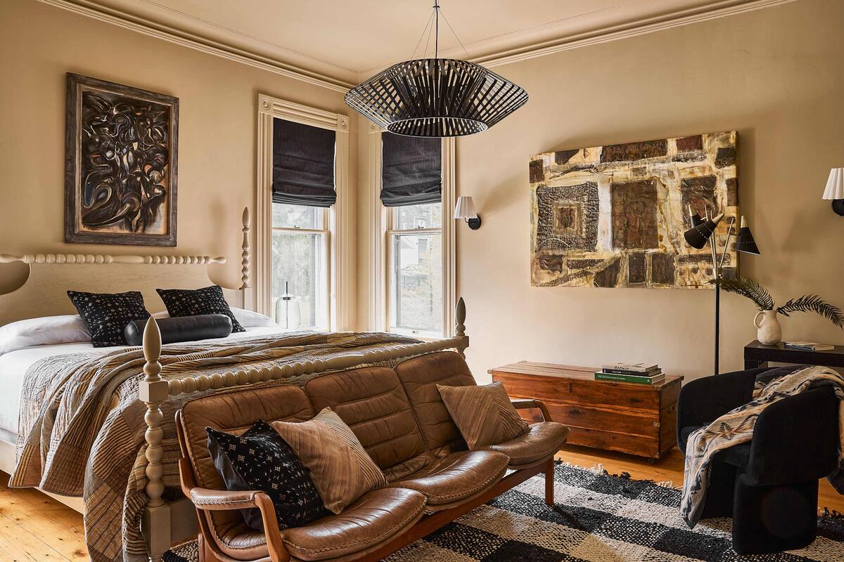 A bedroom with a large bed, a leather sofa, a wooden dresser, and a stone wall artwork.