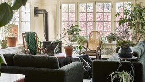 A cozy living room with a checkered floor, two green sofas, a wooden chair, and several potted plants. - Blind Tiger Burlington (Burlington)