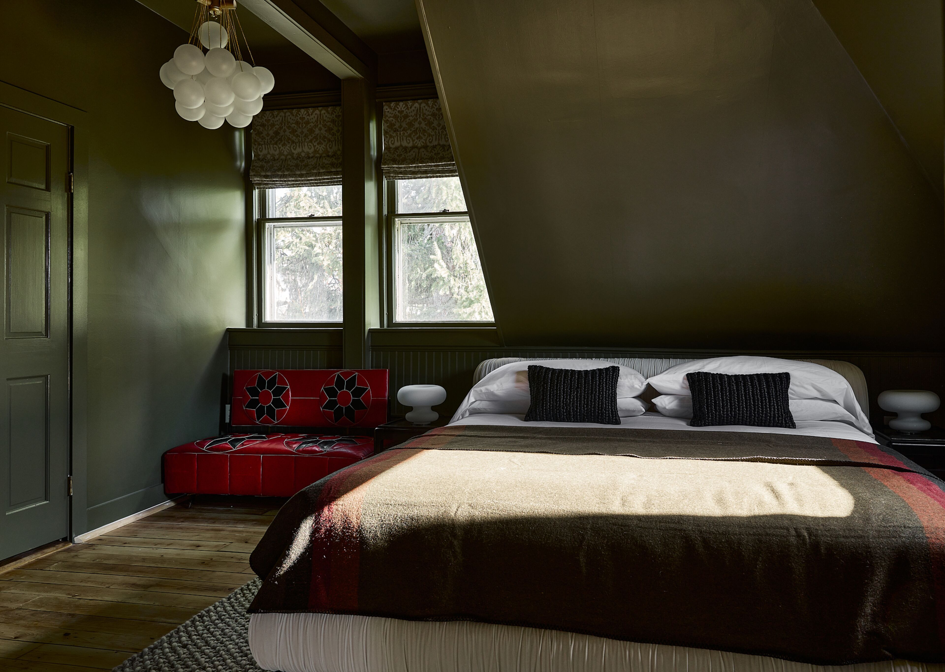 A bedroom with a large bed, a red bench, and a window with a view of trees.