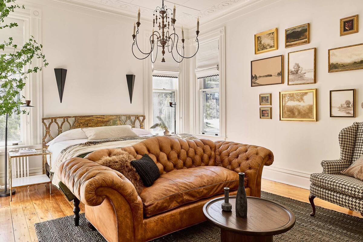 A spacious bedroom with a large bed, a leather sofa, and a chandelier.