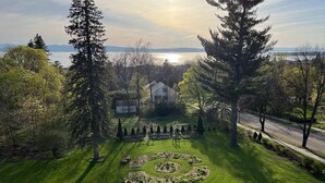 A well-maintained garden with a circular lawn feature, surrounded by tall trees and a view of a body of water in the background. - Blind Tiger Burlington (Burlington)
