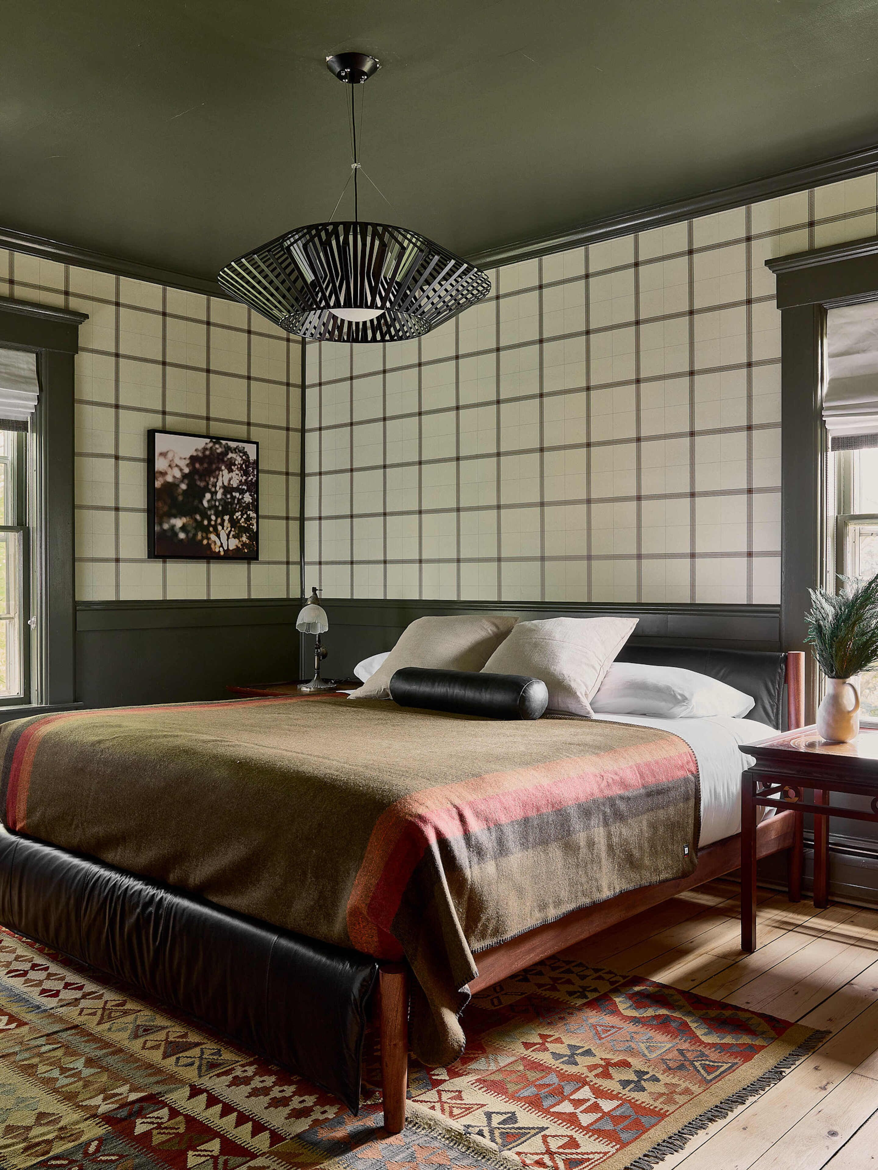Une chambre à coucher avec un grand lit, un tapis à motifs, une table de chevet et un luminaire suspendu.