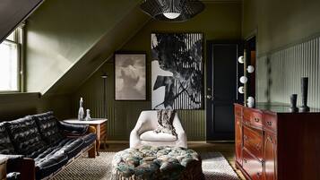 A room with a black leather sofa, a white armchair, a wooden dresser, and a large abstract painting on the wall.