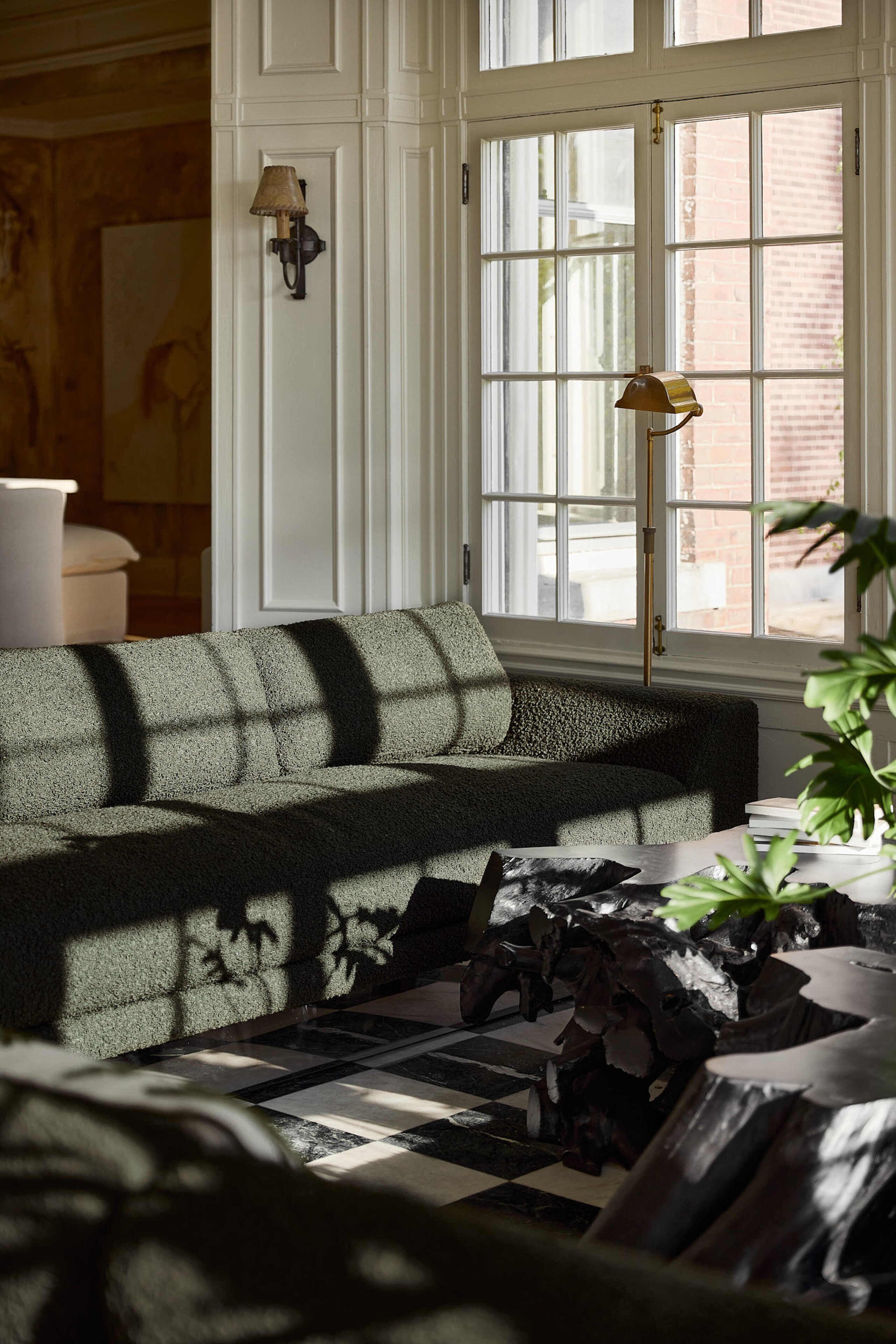 A cozy living room with a sectional sofa, a floor lamp, and a large window with a view of a brick building.
