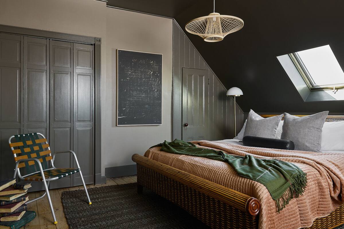 A bedroom with a bed, a chair, a large window, and a ceiling light.