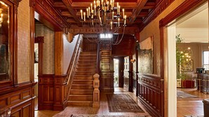 A grand hallway with a wooden staircase, chandeliers, and a large painting on the wall. - Blind Tiger Burlington (Burlington)