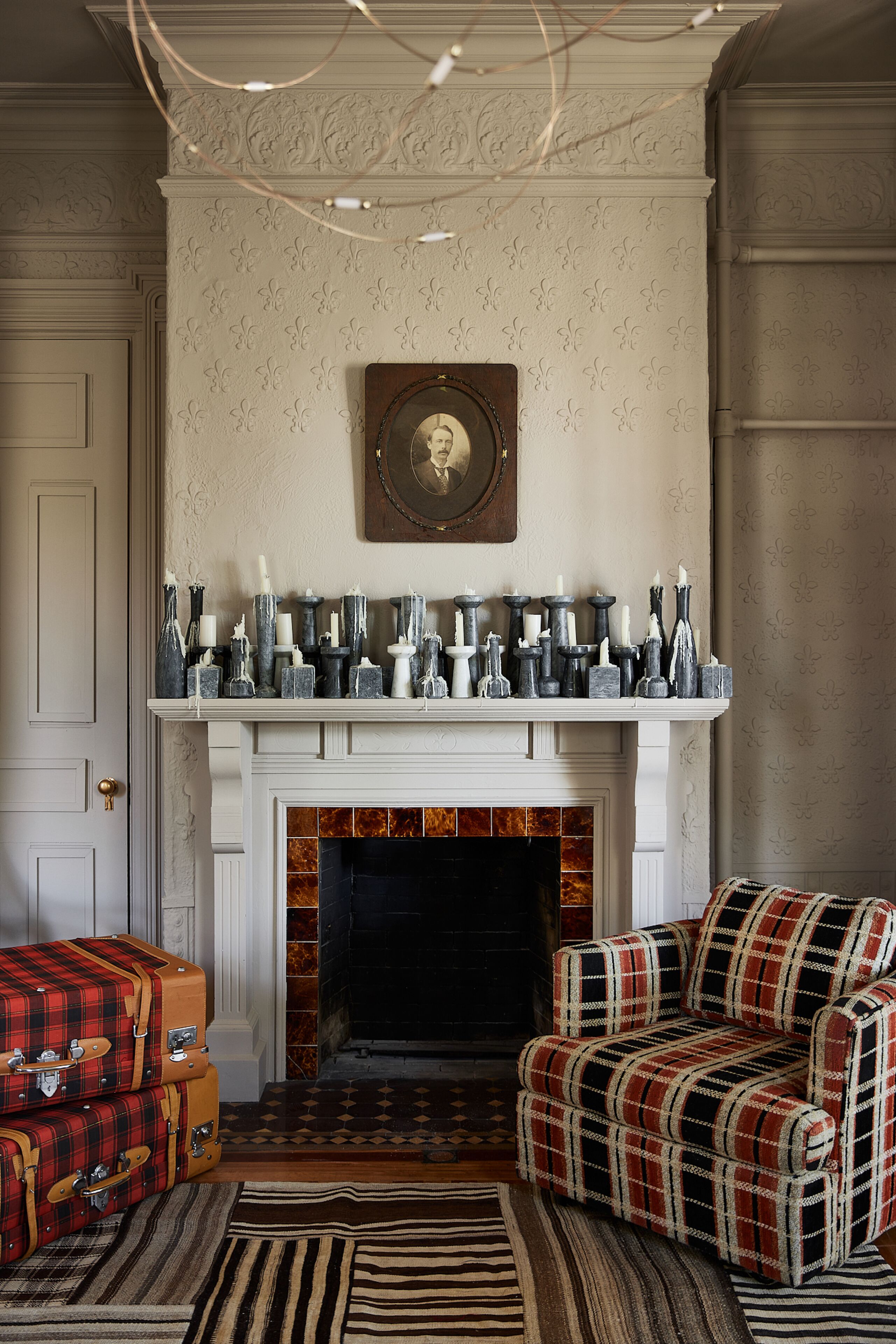 A room with a fireplace, patterned wallpaper, a framed portrait, and a collection of vases on the mantel.