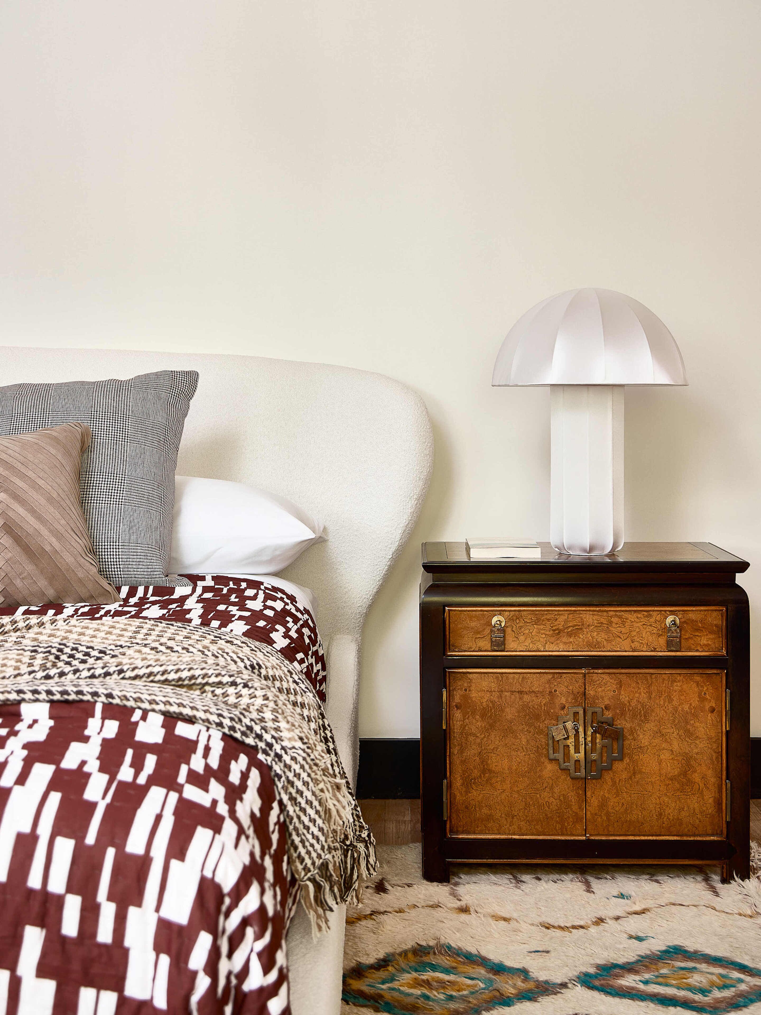 Una cama bien hecha con ropa de cama estampada, una lámpara de noche y una mesita de noche de madera con cajón.
