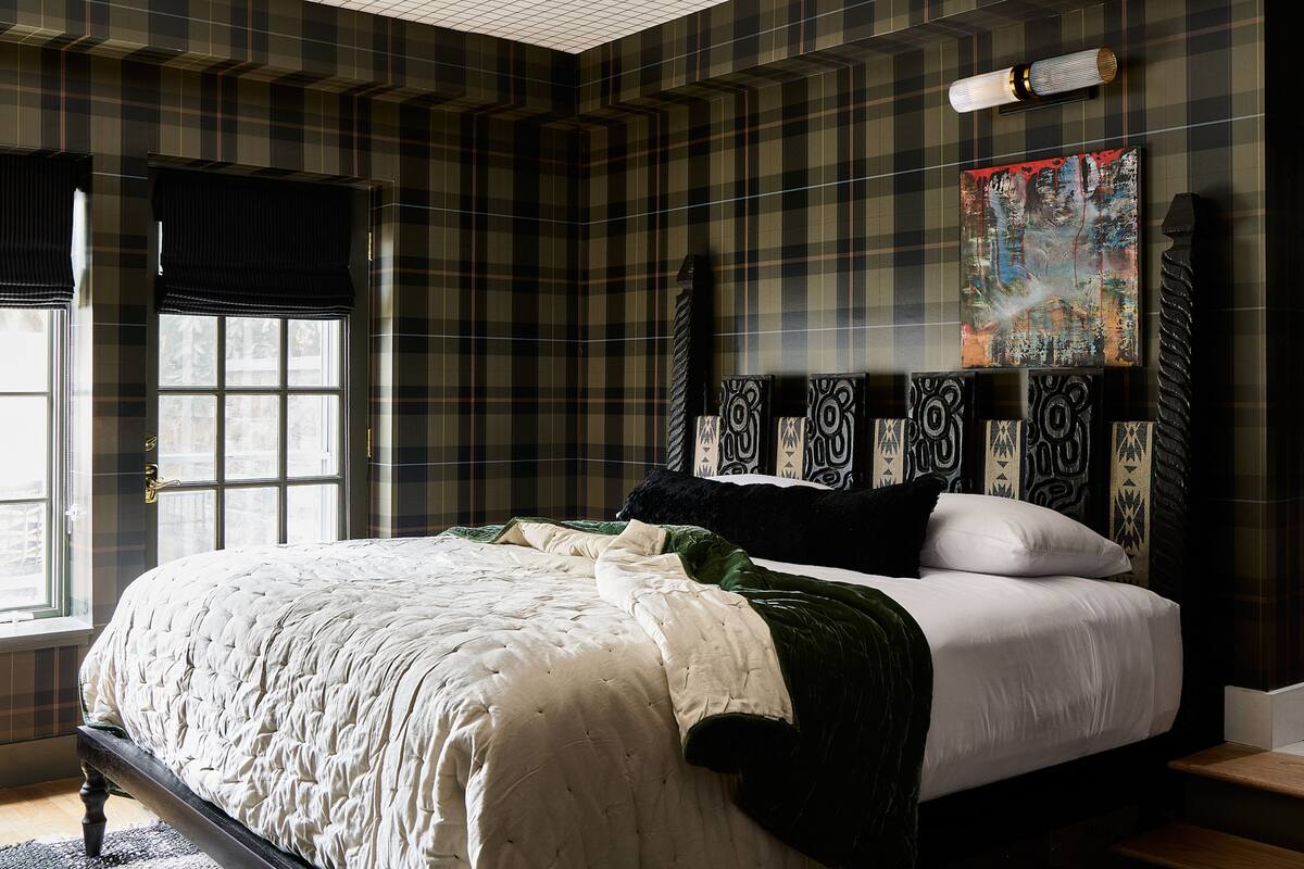 A bedroom with a plaid-patterned wall, a large bed with white bedding, and a painting above the bed.