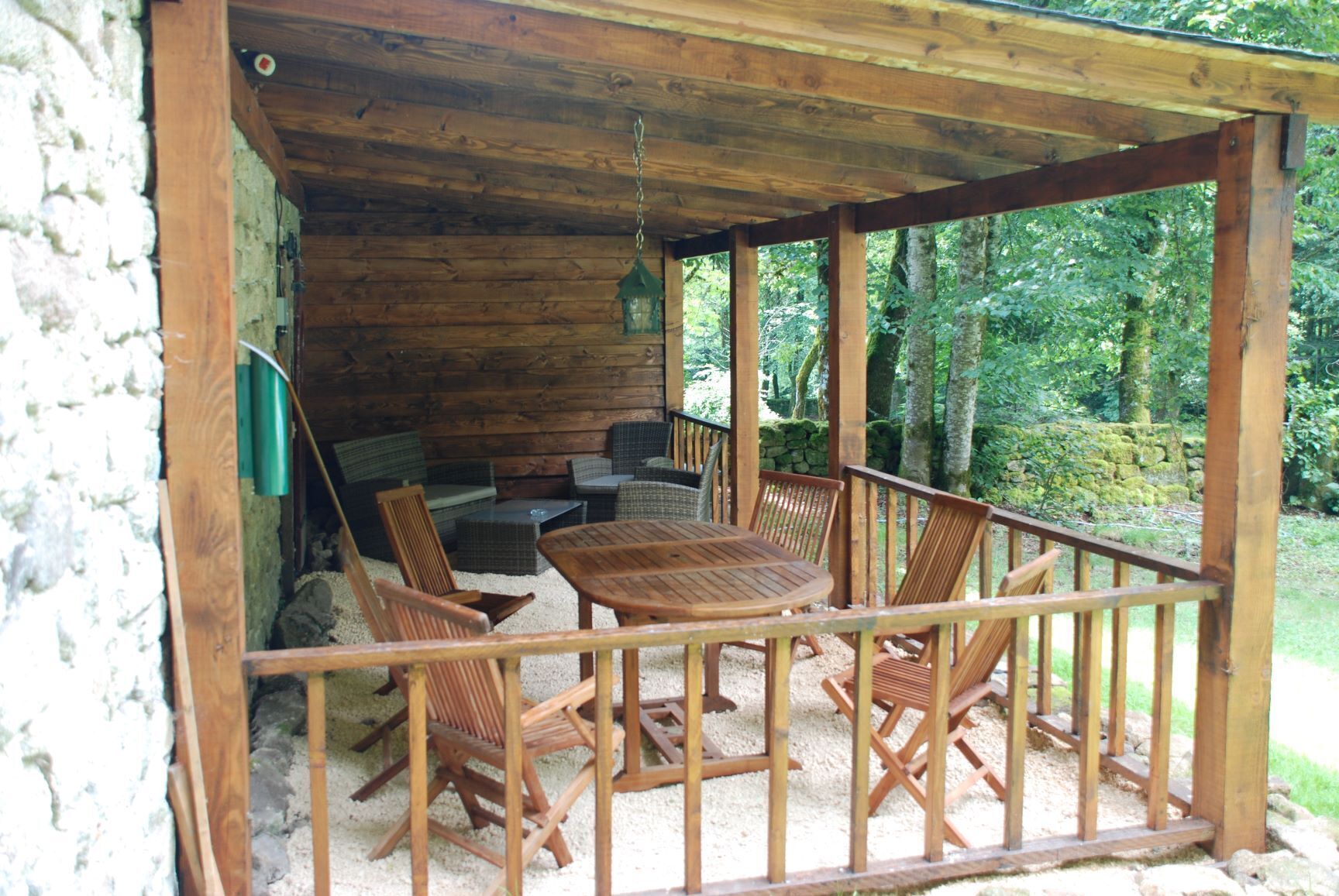 A wooden deck with a table and chairs, surrounded by a stone wall and a wooden fence.