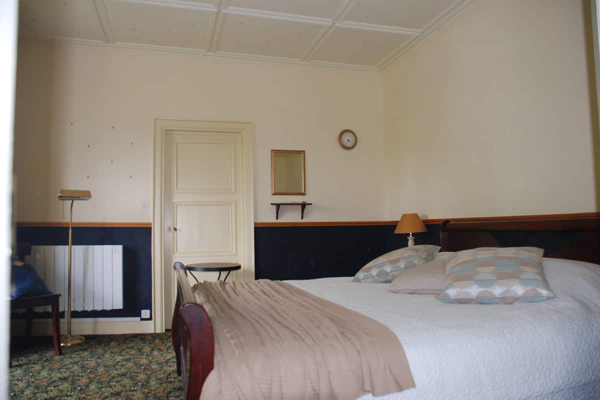 Une chambre à coucher avec un lit, une table de chevet, une lampe et une horloge au mur.