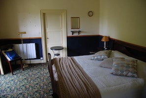 A bedroom with a bed, bedside table, lamp, chair, and a small table with a mirror.