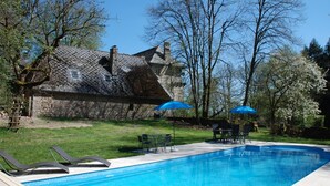 A swimming pool with lounge chairs and umbrellas, surrounded by a stone house and trees.