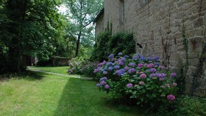 A stone building with a garden path leading to it, surrounded by lush greenery and flowering plants.
