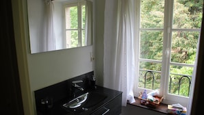 A bathroom with a black sink, a mirror, and a window with a view of greenery.