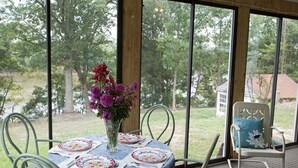 Comedor con una mesa preparada para cuatro personas, sillas alrededor y vistas a una zona boscosa a través de amplios ventanales.