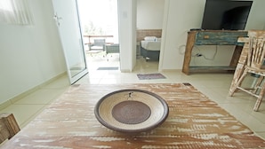 Ein Wohnzimmer mit einem großen, rustikalen Teppich, einem Fernseher auf einem Holzboden und Blick in den Essbereich durch eine offene Tür.