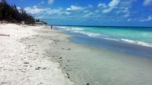 Ein Strand mit klarem türkisblauem Wasser, einem Sandstrand und ein paar Booten in der Ferne.