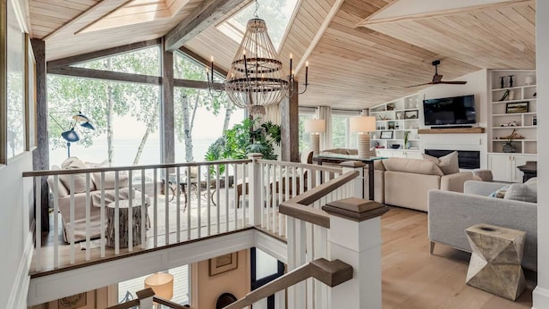 Amplia sala de estar con techo alto, vigas de madera, una escalera y un ventanal con vistas a la vegetación.