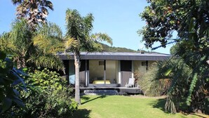 A modern house with a glass facade, surrounded by lush greenery and a clear sky.