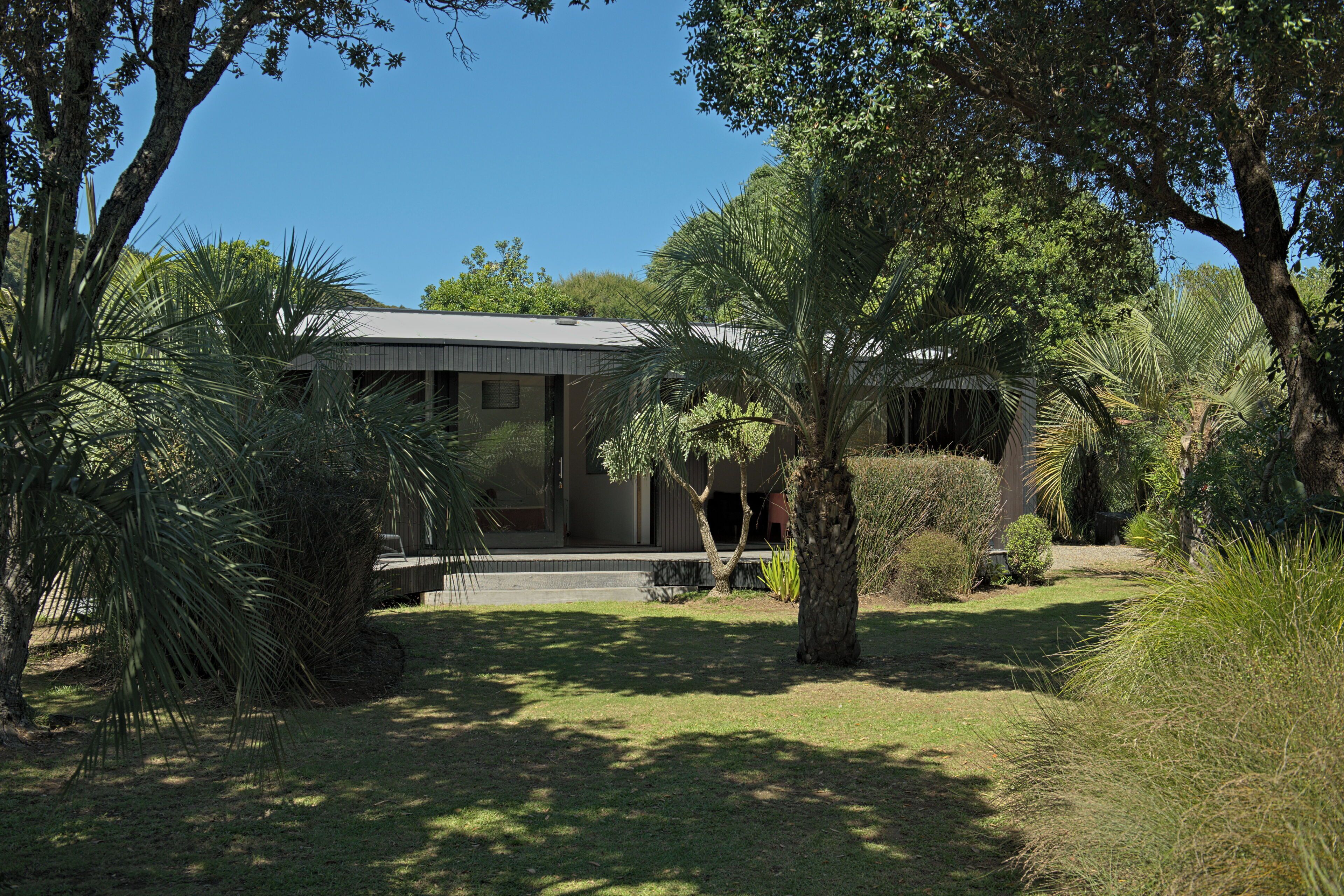 Et moderne hus med en overdækket veranda, omgivet af frodig vegetation og palmer.