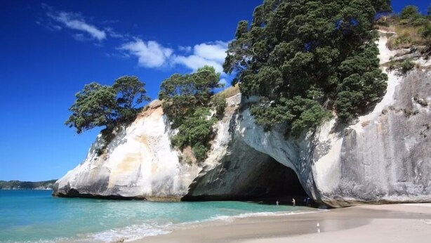 A coastal landscape with a large rock formation, clear blue sky, and turquoise waters.