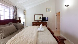 Un dormitorio con una cama grande, un aparador, un televisor y una ventana con cortinas.