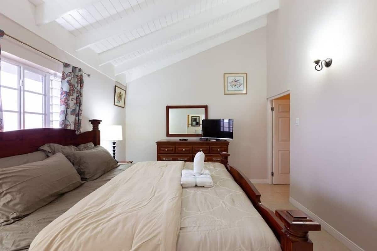 Quarto com cama grande, cómoda, televisão e janela com cortinas.