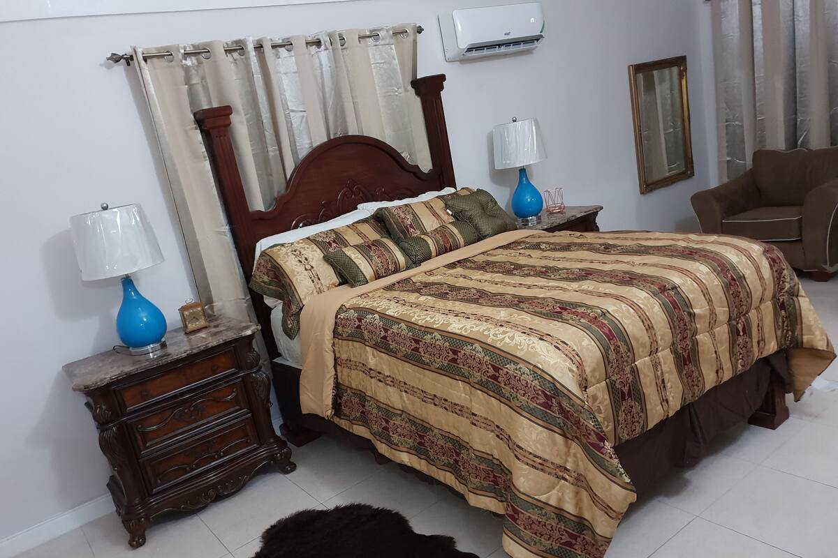Quarto com cama de madeira, duas mesas de cabeceira com luminárias, um espelho e uma cadeira.