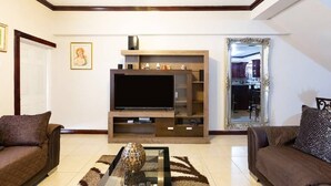 Una sala de estar con una televisión de pantalla plana, dos sofás, una mesa de centro y un espejo decorativo.