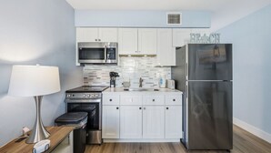 A compact kitchen with white cabinets, a stainless steel refrigerator, a microwave, an oven, and a toaster.