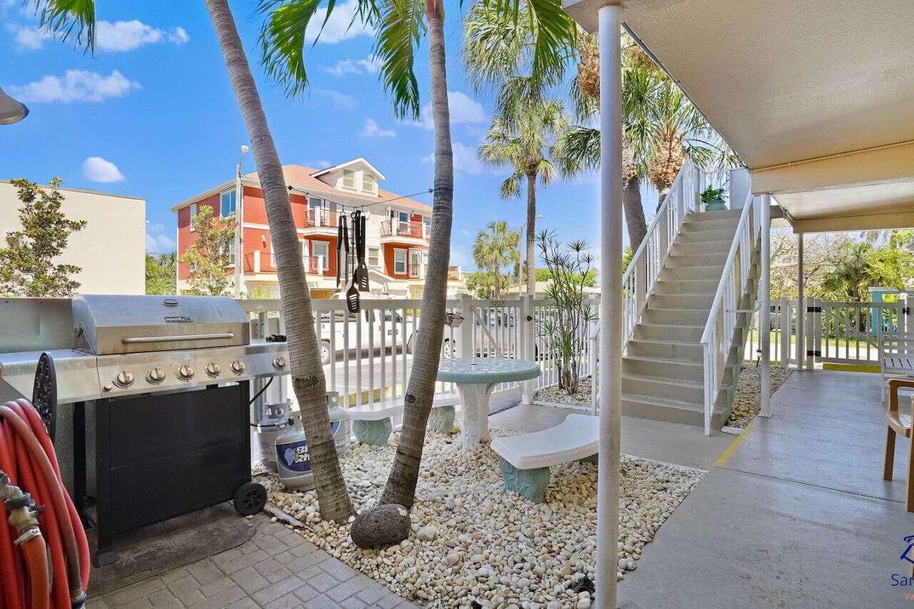 A patio area with a barbecue grill, outdoor seating, and a staircase leading to a covered deck.