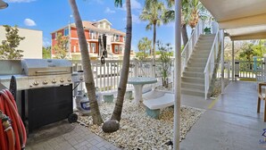 A patio area with a barbecue grill, outdoor seating, and a staircase leading to a covered deck.