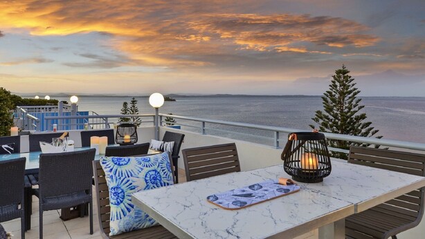 Un área de estar al aire libre con vista al mar, que incluye una mesa, sillas y faroles decorativos.