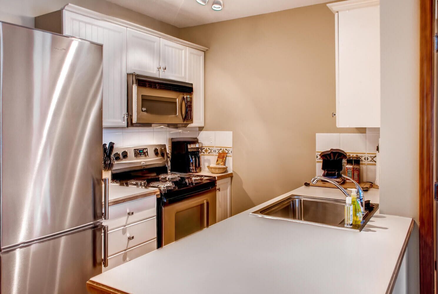 A modern kitchen with stainless steel appliances, white cabinetry, and a central island with a sink.