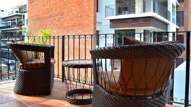 Wicker chairs with cushions on a balcony with a view of a brick building and other apartments.