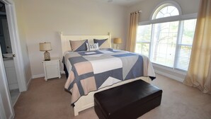 A bedroom with a large bed, two bedside tables, a bench, a ceiling fan, and a window with curtains. - Cypress Bend Apartment 532 (North Myrtle Beach)