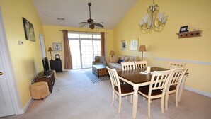 A dining area with a table and chairs, a sofa, and a ceiling fan. - Cypress Bend Apartment 532 (North Myrtle Beach)