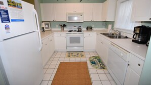 A kitchen with white cabinets, a microwave, stove, and a dishwasher. There are two shark decorations on the wall. - Cypress Bend Apartment 532 (North Myrtle Beach)